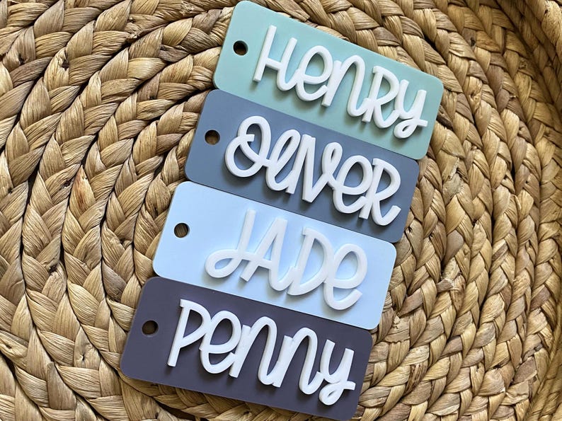 Peut inclure: Quatre porte-cl&eacute;s rectangulaires en acrylique avec des noms diff&eacute;rents &eacute;crits en lettres cursives blanches. Les noms sont Henry, Oliver, Jade et Penny. Les porte-cl&eacute;s sont dans des tons de bleu et de gris.