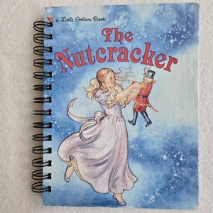 May include: A spiral-bound book titled "The Nutcracker" with a blue cover featuring an illustration of a woman in a flowing dress holding a toy soldier. The text "a Little Golden Book" is at the top.