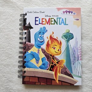 May include: A spiral-bound notebook featuring the Disney Pixar Elemental movie cover art. The front shows a blue water character and a flame character sitting on a ledge with a city skyline in the background. The text reads A Little Golden Book and Elemental.