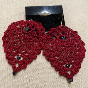May include: A pair of red crocheted heart-shaped earrings with black bead accents.