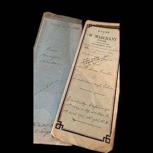 May include: Two vintage legal documents with cream and light blue paper covers. The cream document features black printed text reading ETUDE M MARCHANT NOTAIRE and handwritten cursive notes dated 1920. The blue document has handwritten text.
