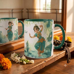 May include: A white ceramic mug with a dark green handle and rim, featuring an illustration of a person in a teal and gold traditional dance costume. The design includes the word Text in script font and a background of green foliage and water.