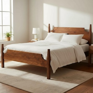 May include: A wooden bed frame with a headboard and footboard. The bed is made of dark brown wood and has white bedding. A white lamp sits on a nightstand next to the bed. A rug is on the floor.