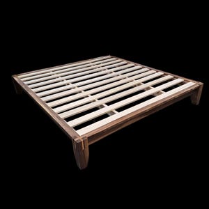May include: A wooden bed frame with a dark brown finish and a slatted design. The frame has a rectangular shape with four sturdy legs. The bed frame is made of wood and is designed to support a mattress.