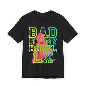 May include: Black t-shirt featuring a graphic of a person in a colorful outfit with the text "BAD BUNNY BOWL LX" in a neon gradient. The design is centered on the front of the shirt.
