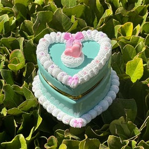Caja de baratijas con forma de corazón de pastel falso con lazos rosas, perlas y macarrones en la parte superior