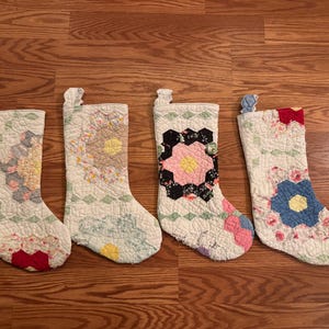 May include: Four white quilted Christmas stockings with different floral patterns. The stockings are decorated with pink, blue, red, and black flowers.