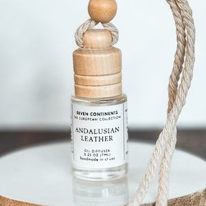 May include: A small glass bottle with a wooden cap and a string for hanging. The bottle contains a clear liquid and has a label that reads "Seven Continents The European Collection Andalusian Leather Oil Diffuser 0.25 oz (7ml) Handmade in USA".