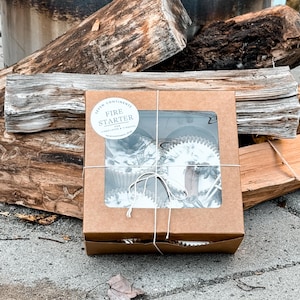 May include: A brown cardboard box with a clear window showing fire starter logs inside. The box is tied with twine and has a white label that says "Fire Starter for Fireplaces & Firepits".