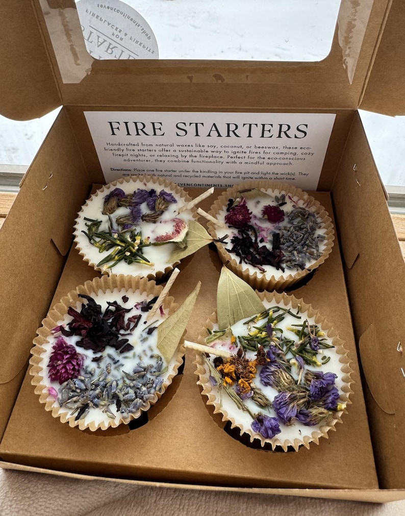 May include: Four fire starters in a cardboard box. The fire starters are made of natural waxes like soy, coconut, or beeswax. They are decorated with dried flowers and herbs. The box has the text "FIRE STARTERS" printed on it.