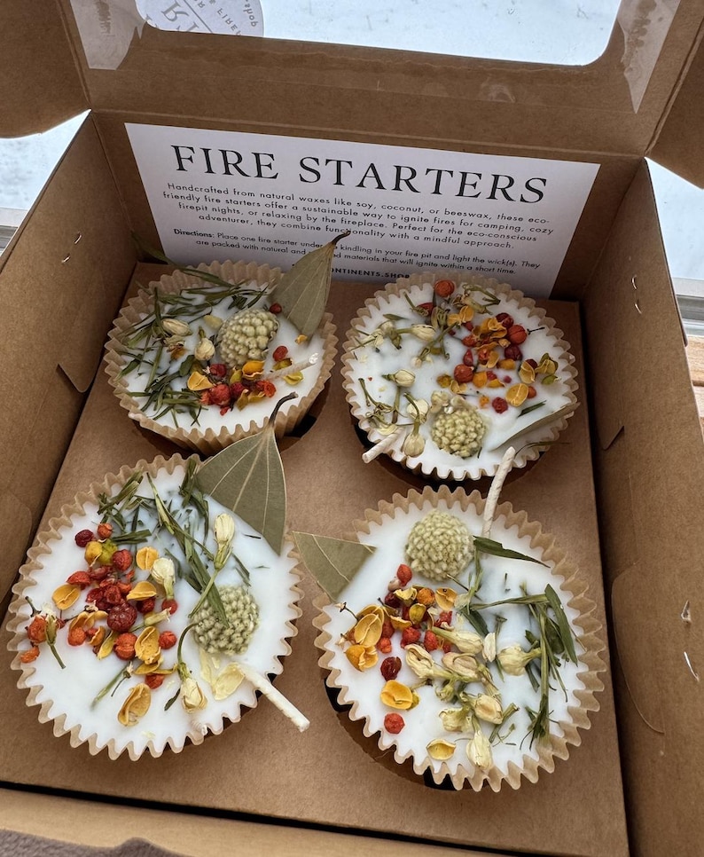 May include: Four white fire starters in paper cups with dried flowers and herbs. The fire starters are made with natural waxes like soy, coconut, or beeswax. The text on the box reads "Fire Starters".