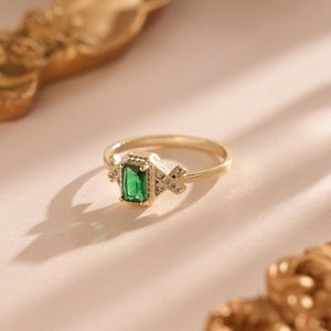 Peut inclure: Une bague en or avec une émeraude verte et de petites pierres claires serties dans un motif géométrique.