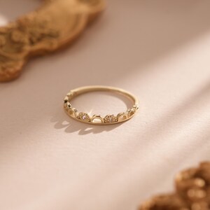 Può includere: Un delicato anello d'oro con un design unico caratterizzato da piccoli archi e pietre scintillanti.