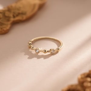 Könnte beinhalten: Ein zarter Goldring mit kleinen, klaren Steinen, die in einem schlichten Band gefasst sind.