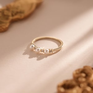Peut inclure: Une bague en or avec une rangée de cinq petites perles blanches et de minuscules pierres claires.