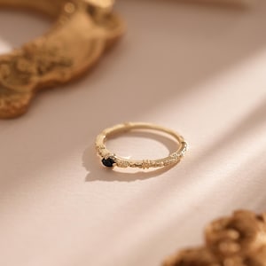 Puede incluir: Un anillo de oro con una banda texturizada y una peque&ntilde;a piedra negra en el centro.