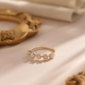 Può includere: Un anello d'oro con cinque pietre di opale bianco incastonate in una fascia delicata.