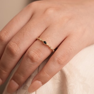 Puede incluir: Un delicado anillo de oro con una piedra preciosa negra engastada en el centro. El anillo est&aacute; hecho de una banda texturizada.