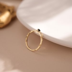 Puede incluir: Un anillo de oro con una banda delicada y texturizada y una peque&ntilde;a piedra preciosa negra en el centro.