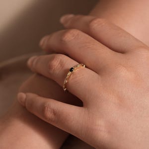 Puede incluir: Un delicado anillo de banda de oro con una piedra preciosa negra y peque&ntilde;as piedras blancas engastadas en un dise&ntilde;o floral.