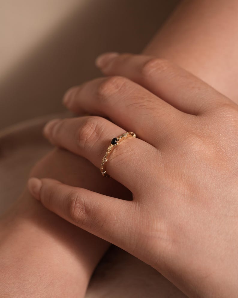 Puede incluir: Un delicado anillo de banda de oro con una piedra preciosa negra y peque&ntilde;as piedras blancas engastadas en un dise&ntilde;o floral.