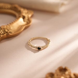 Puede incluir: Un anillo de oro con una banda texturizada y una peque&ntilde;a piedra preciosa negra en el centro.