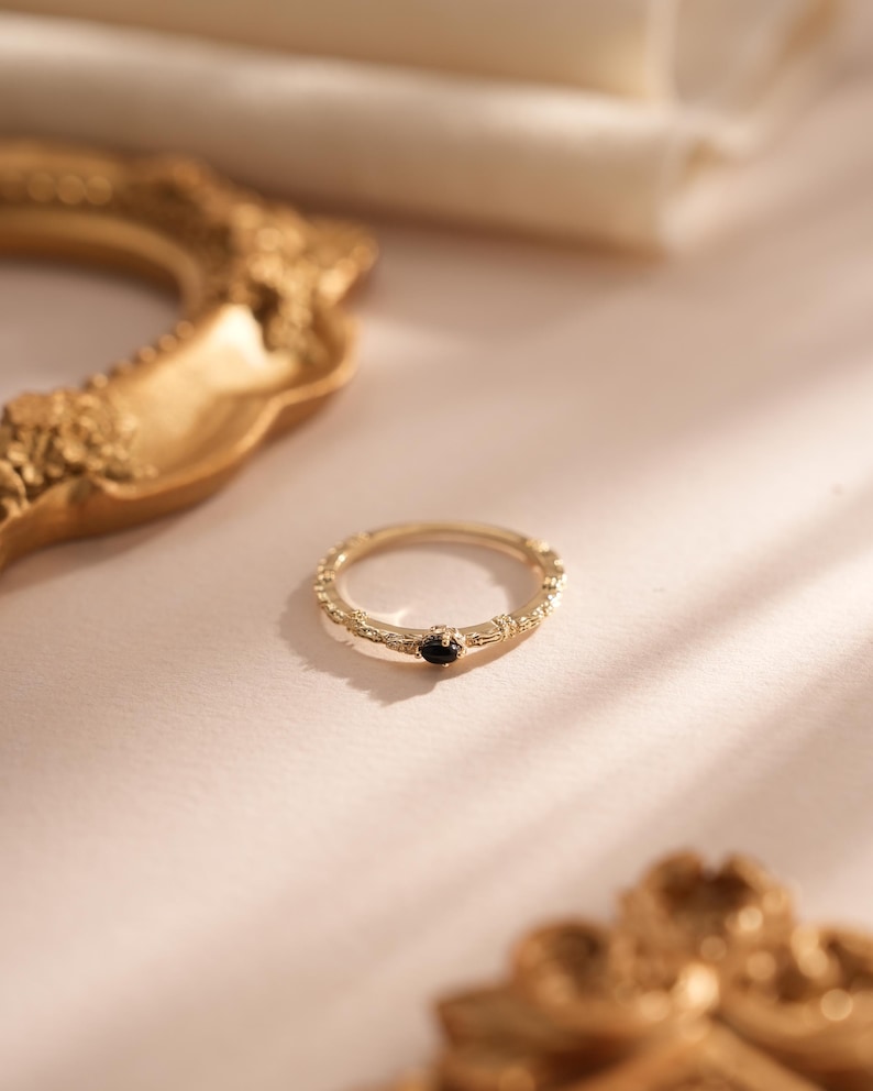 Puede incluir: Un anillo de oro con una banda texturizada y una peque&ntilde;a piedra preciosa negra en el centro.