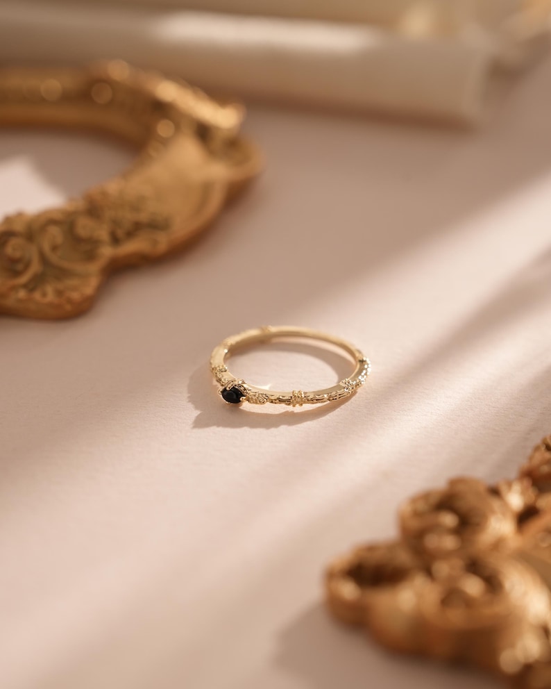 Puede incluir: Un anillo de oro con una banda texturizada y una peque&ntilde;a piedra negra en el centro.