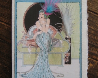 May include: A vintage-style greeting card featuring a woman in a blue and silver sequined dress sitting on a couch. She is wearing a feathered headpiece and has a glamorous look. The card has a blue border and a white background.