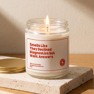 May include: A clear glass jar candle with a lit wick and white wax. The label features a red border and red text that reads: Smells Like They Declined Diagnostics but Want Answers. It also states 100% Soy Wax Candle Handpoured in California.