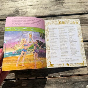 Pode incluir: Livro aberto com ilustra&ccedil;&otilde;es coloridas. Uma p&aacute;gina mostra duas mulheres numa praia, segurando um trof&eacute;u. A outra p&aacute;gina lista t&iacute;tulos. O livro tem uma borda rosa e o texto "Little Golden Book".