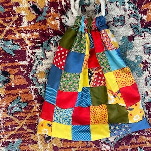 May include: A colorful patchwork drawstring bag with a variety of floral, geometric, and polka dot patterns in red, blue, yellow, and green.