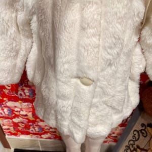 May include: A white, fluffy coat with a single button closure. The coat has long sleeves and a soft, textured appearance. The garment appears to be made of a plush material, possibly faux fur.