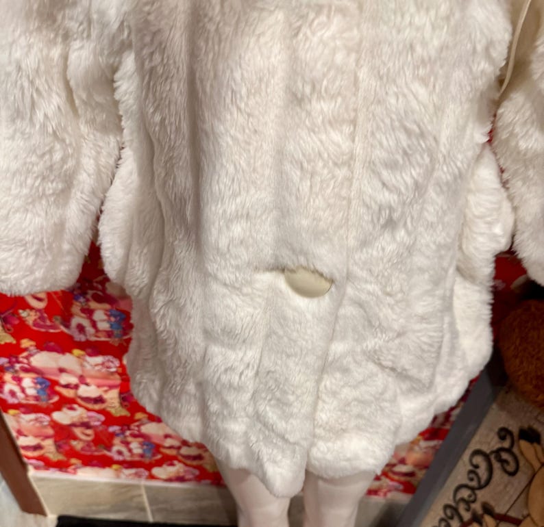 May include: A white, fluffy coat with a single button closure. The coat has long sleeves and a soft, textured appearance. The garment appears to be made of a plush material, possibly faux fur.
