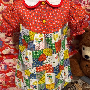 May include: A vintage-style dress with a red floral bodice and patchwork skirt. The dress features a white collar with red trim, yellow buttons, and short, puffed sleeves. The patchwork skirt has various colorful patterns.
