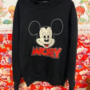 Op de afbeelding: Zwart sweatshirt met een rode Mickey Mouse-afbeelding en het woord "MICKEY" in rode letters.