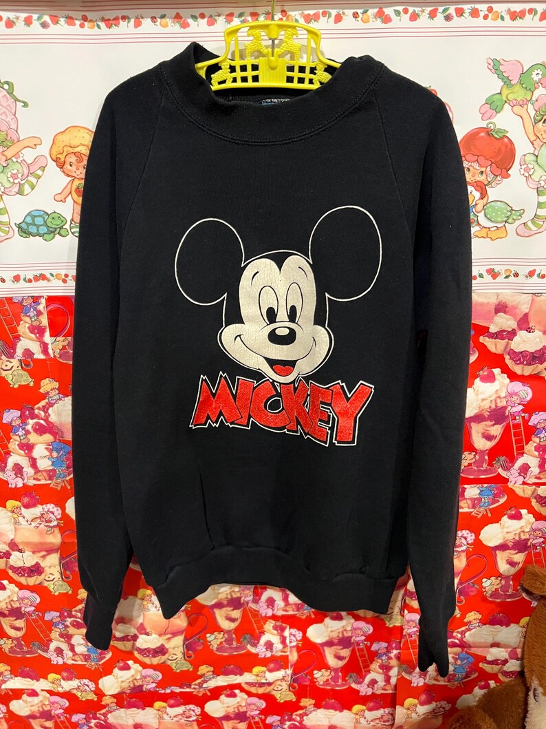 Op de afbeelding: Zwart sweatshirt met een rode Mickey Mouse-afbeelding en het woord "MICKEY" in rode letters.