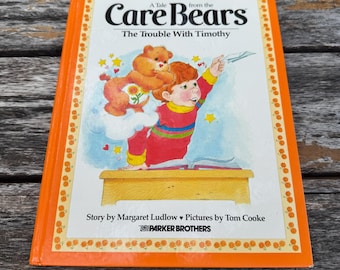 May include: A vintage Care Bears book titled "The Trouble With Timothy" with an orange border. The cover features a cartoon illustration of a Care Bear and a child. The book is by Margaret Ludlow and Tom Cooke.