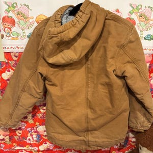 Puede incluir: Chaqueta con capucha marr&oacute;n con forro polar gris. La chaqueta tiene cierre de cremallera completo y m&uacute;ltiples bolsillos. La capucha es grande y est&aacute; forrada con el mismo material de forro polar gris. La chaqueta est&aacute; hecha de tela duradera estilo workwear.