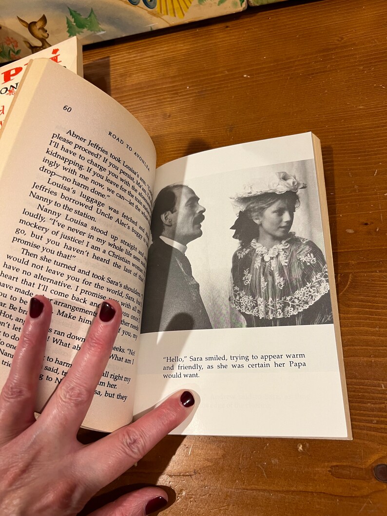 May include: A vintage book open to a page with a black and white photo of a man and a young girl. The book is titled "Road to Avonlea". The text on the page reads "Abner Jeffries took Louisa's arm. "I'll have to charge you with the serious offense of kidnapping. If you leave for the train willingly with me now, we can let the whole thing drop - no harm done."