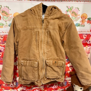 Puede incluir: Chaqueta con capucha de color marr&oacute;n claro con cremallera completa. Cuenta con dos bolsillos delanteros grandes, dos bolsillos en el pecho y un parche con el logotipo de Carhartt. Fabricada en tejido resistente de estilo trabajo.