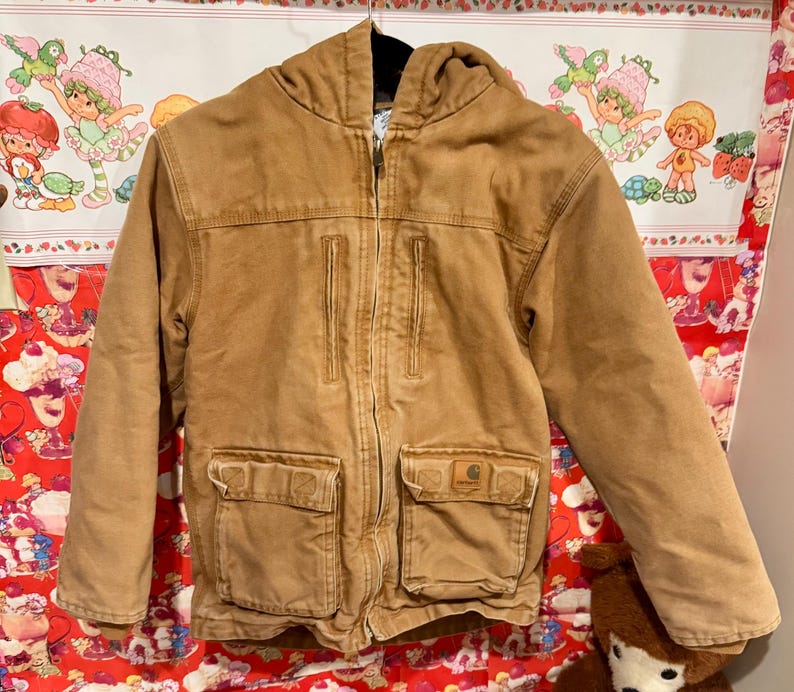 Puede incluir: Chaqueta con capucha de color marr&oacute;n claro con cremallera completa. Cuenta con dos bolsillos delanteros grandes, dos bolsillos en el pecho y un parche con el logotipo de Carhartt. Fabricada en tejido resistente de estilo trabajo.