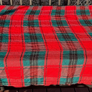 Puede incluir: Una manta grande y rectangular a cuadros rojos y verdes. La manta presenta un patrón de tartán clásico con rayas rojas y verdes audaces, creando un diseño visualmente impactante. La tela parece suave y posiblemente tejida.