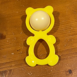 May include: Yellow plastic baby rattle shaped like a bear with a white ball in the center.