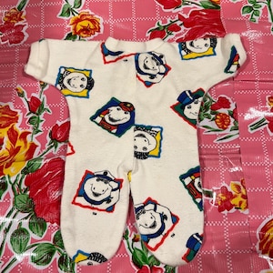 May include: White baby onesie with a colorful cartoon print of a hippopotamus wearing different hats and outfits. The onesie has a long sleeve and a snap closure.