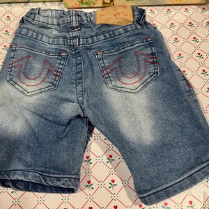 以下が含まれることがあります： バックポケットに赤いステッチが入った青いデニムショーツ。 ショーツは色あせたウォッシュ加工で、ウエストバンドには茶色の革パッチが付いています。 バックポケットには、特徴的な赤いステッチのデザインが施されています。