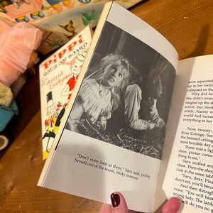 May include: A close-up of a book open to a page with a black and white photo of a young girl with a worried expression. The text on the page reads "Don't even look at them," Sara said, pulling herself out of the warm, sticky manure."