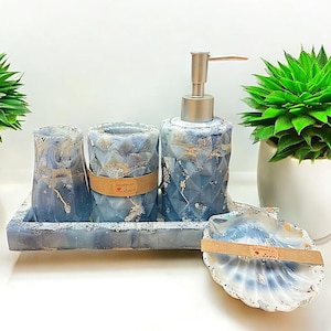 Könnte beinhalten: Ein Badezimmer-Set mit einem Seifenspender, zwei Bechern und einer Seifenschale. Das Set ist aus Beton und hat ein blaues und weißes Marmormuster. Der Seifenspender hat eine silberne Pumpe. Die Seifenschale ist muschelförmig.