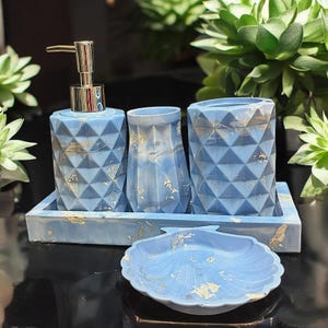 Könnte beinhalten: Ein blaues Badezimmer-Set mit geometrischem Design. Das Set beinhaltet einen Seifenspender, einen Becher, einen Zahnbürstenhalter, ein Tablett und eine muschelförmige Schale. Goldblatt-Akzente sind über das Set verstreut.