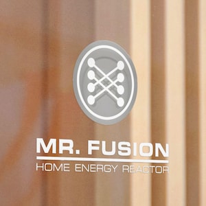 Puede incluir: Una puerta de cristal transparente con el texto "MR. FUSION HOME ENERGY REACTOR" y un logotipo circular. El logotipo es un diseño blanco dentro de un círculo gris. El fondo presenta paneles de madera verticales.